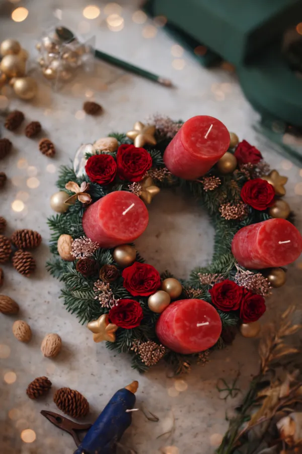 Adventní věnec z jedle nobilis ozdobený červenými svíčkami, růžemi, šiškami a zlatými ozdobami